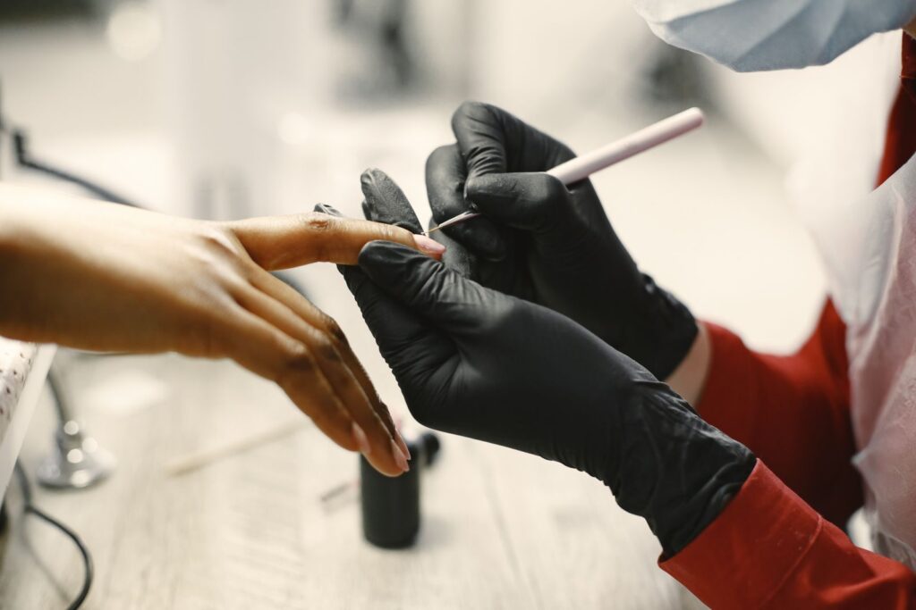 Nail technician wearing black gloves performing a professional manicure with sterilised tools